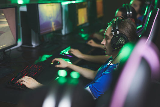 Group of serious young men in headsets sitting in line and using computers while playing pc games in computer club